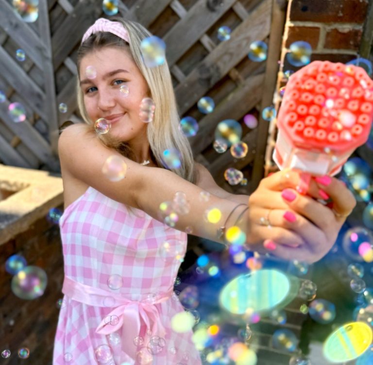 Barbie theme kids' party Young woman in a pink checkered dress blowing bubbles with a bubble gun.